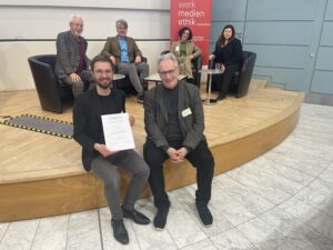 Der Preisträger Stefan Kosak (u.l.) neben dem Juryvorsitzenden Christian Schicha. Im Hintergrund (v.l.n.r.) Jury-Mitglied Rüdiger Funiok, die Fachgruppensprecher:innen Lars Rademacher und Claudia Paganini und Jury-Mitglied Laura Martena.